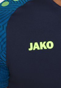 Marinefarbenes Sportshirt mit blauen Streifenakzenten. Über dem Brustbereich befindet sich das leuchtend grüne "JAKO"-Logo. Weicher, strukturierter Stoff.