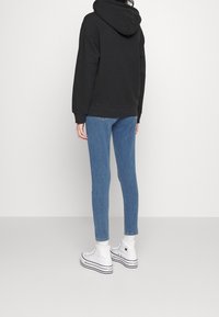Sweat à capuche noir, jean skinny bleu, et baskets montantes blanches. La tenue présente une coupe décontractée et des éléments de design basiques.
