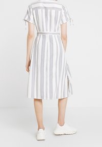 Randig klänning i vitt och marinblått, kortärmad, cinchad midja, medellång med en sidoklyvning, i kombination med vita sneakers.