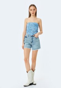 Strapless blauwe top met paisleypatroon, gecombineerd met lichtgewicht denim shorts en witte cowboylaarzen met decoratieve stiksel.