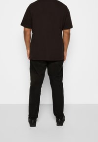 Sort kortærmet t-shirt lavet af bomuld, parret med sorte tapered bukser. Stoffet fremstår glat med et enkelt, ensfarvet design.