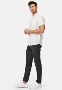 Camisa de lino blanca de manga corta con un bolsillo en el pecho, combinada con pantalones oscuros ajustados en gris y zapatillas blancas.