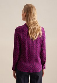 Maglietta viola a maniche lunghe con motivo geometrico, tessuto morbido e polsini abbottonati, orlo dritto e vestibilità sagomata.