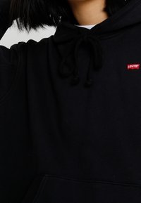 Sweat à capuche noir en tissu doux, avec une poche kangourou à l'avant, une capuche réglable à cordon, et un petit logo rouge Levi's sur la poitrine.