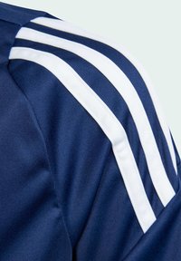 Tumši zila sporta krekls ar trim baltām svītrām uz pleca, izgatavots no gludas, elpojošas auduma.