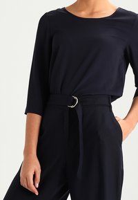 Maglietta lunga blu navy con scollatura rotonda, abbinata a pantaloni a vita alta con una cintura larga e una fibbia metallica circolare.