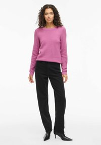 Różowy sweter dziany z teksturowanym wzorem, okrągłym dekoltem i długimi rękawami, zestawiony z czarnymi, wysokim stanem dżinsami i czarnymi, spiczastymi szpilkami.