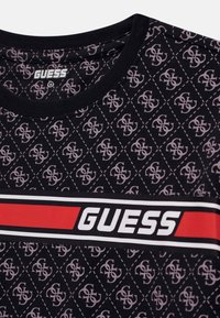Svart bomulls t-shirt med ett upprepat logomönster i ljusrosa, med en djärv röd och vit "GUESS"-logotyp över bröstet.
