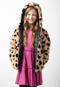 Kurtka z futra syntetycznego w leoparda z czarnym ocieplanym wnętrzem, z różowymi zamkami błyskawicznymi, noszona na różowej sukience z plisami i falbaniastym dołem.