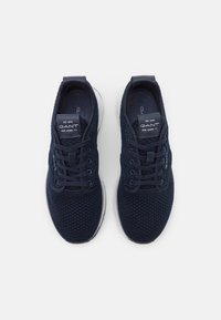 Mörkblå stickade sneakers med ett andningsbart material, utrustade med en vit sula, snörning och märke på tungan.