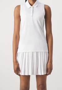 Bílý bezrukávový polo top s knoflíkovou légou, který je kombinován s plisovanou bílou sukní. Hladká tkanina a přiměřený střih. Drobný detail loga na boku.