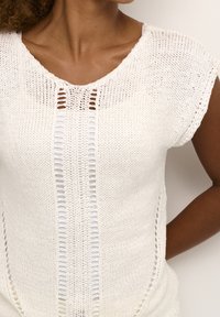 Vit stickad topp med V-hals, korta ärmar och vertikal öppen vävning längs fram, med en mjuk, strukturerad yta.