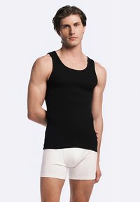 Black tank top with a round neckline, fitted design, and smooth texture; paired with white boxer shorts. Simple, minimalistic style.