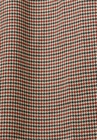 Motif de tissu pied-de-poule marron, noir et blanc avec une surface légèrement texturée et des plis doux.