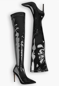 Černé lakované kozačky až ke stehnům s špičatými špičkami, stiletto podpatky a bočním zipem na jedné z bot, zobrazené na bílém pozadí.