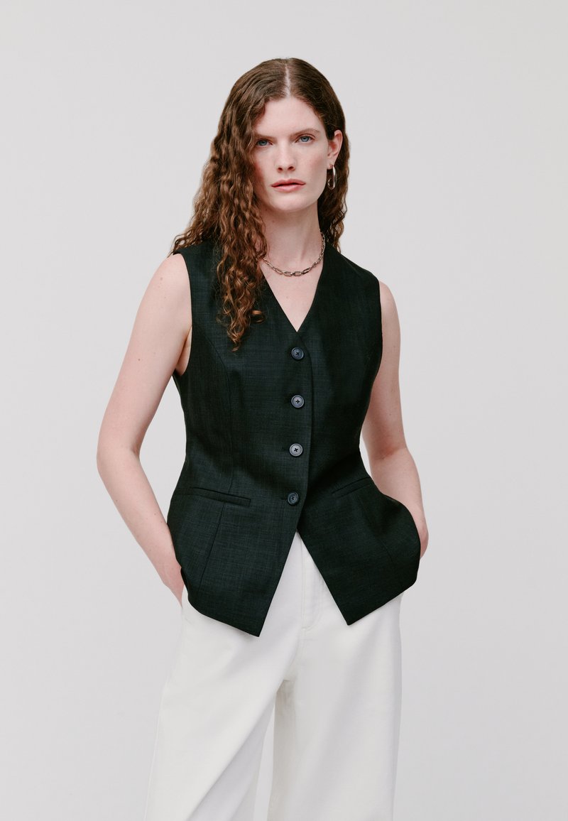 Ärmellose schwarze Weste mit V-Ausschnitt, fünf vorderen Knöpfen und seitlichen Taschen; glatte Textur mit einem subtilen Gewebemuster.