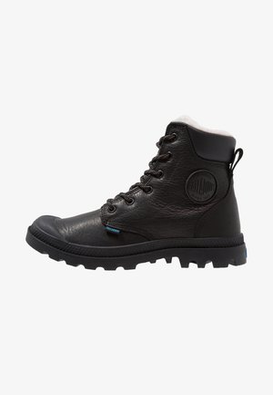 Bottine montante en cuir noir avec col rembourré, fermeture avant à lacets, semelle épaisse crantée et logo rond Palladium sur le côté.