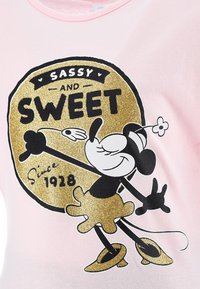 Camiseta de algodón rosa con un gráfico en negro y dorado de un personaje de dibujos animados con un detalle floral, texto que dice "SASSY AND SWEET" y "Desde 1928."
