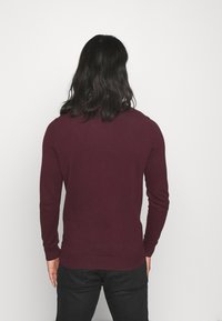Dunkelroter Pullover mit langen Ärmeln, gerippten Bündchen und Saum, aus weichem Material. Einfaches Design ohne sichtbare Muster oder Akzente.