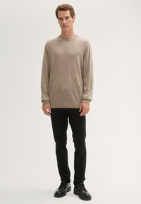 Helle braune, langärmelige Strickjacke mit rundem Halsausschnitt, kombiniert mit schwarzen Slim-Fit-Hosen und schwarzen Schnürschuhen.