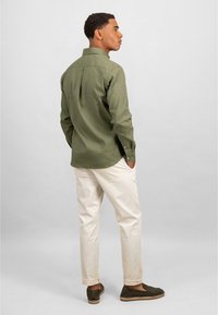 Olijfgroen overhemdd met lange mouwen, rugpand, gebogen zoom en witte katoenen broek. Draag het met donkergroene espadrilles.