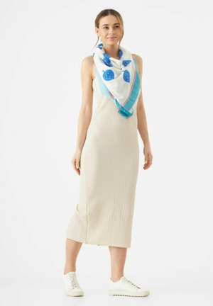 Beiges Midi-Kleid aus strukturiertem Stoff, akzentuiert mit einem blau-weißen Schal mit Erdbeer-Muster und einem lebhaften Rand. Weiße Sneakers runden den Look ab.
