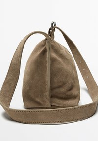 Borsa in suede marrone con forma arrotondata, chiusura zip e tracolla regolabile. La texture è morbida, con cuciture visibili lungo i bordi.