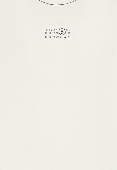 Maglietta bianca in morbido cotone, con scollo rotondo e un'etichetta con motivo a griglia e il numero 6 stampato in un cerchio.