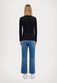 Zwarte top met lange mouwen gecombineerd met blauwe wijde jeans. De jeans hebben achterzakken en rafelige zoom, compleet met witte schoenen.