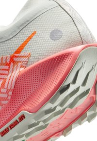 Scarpa sportiva grigia con upper testurizzato, accenti arancioni brillanti, tallone rosa e suola robusta con rilievi ben definiti e branding Nike Trail ATC.