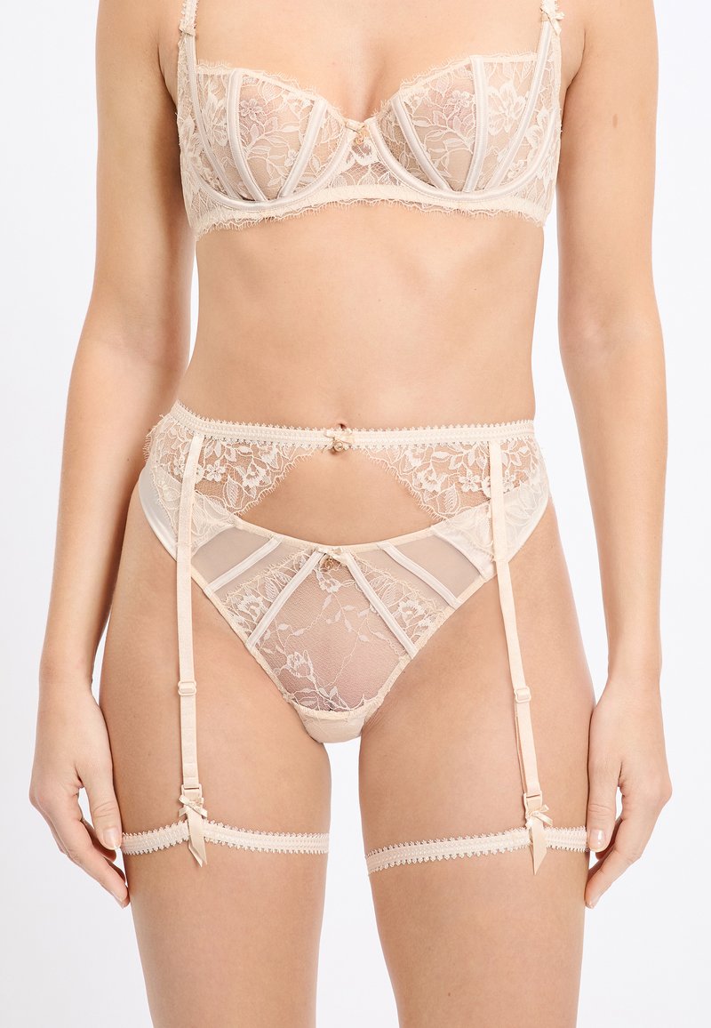 Lingerieset van kant in naaktkleur met doorschijnende mesh panelen. Voorzien van beugelbeha, jarretelriem en decoratieve bandjes. Delicate bloemmotieven.