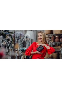 Black leather wallet with a quilted design, featuring a silver accent. Displayed in hands against a background of decorative items.