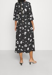 Svart klänning med vita abstrakta mönster, mittlång, med ett bälte och trekvartsärmar. Mjuk tyg med dragkedja på baksidan.