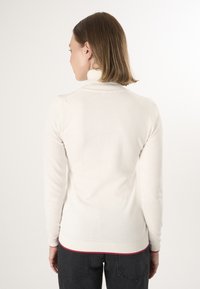 Witte coltrui met een ribbelstructuur bij de hals en mouwen, voorzien van een contrasterende rode rand aan de onderkant. Zachte textuur, aansluitend ontwerp.