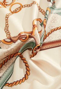 Foulard en soie avec un fond crème, présentant un motif de chaîne et de cordeaux en tons dorés et verts, affichant des détails complexes et une texture lisse.