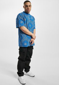 Blå mønstrete kortermet skjorte med bandana-design, kombinert med svarte cargo-bukser og hvite sneakers. Har en avslappet passform.
