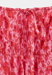 Tissu floral rouge et rose avec une bande élastique froncée et un cordon noué au centre.