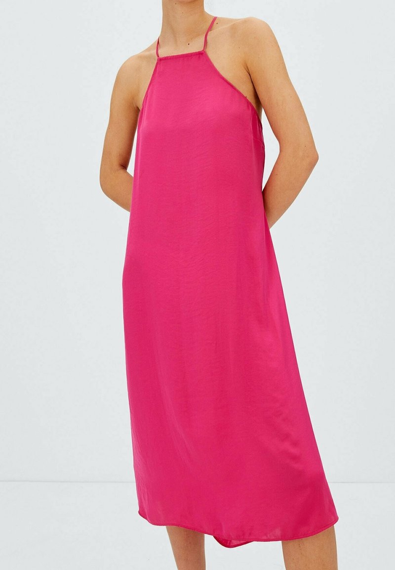 Robe midi rose vif sans manches avec fines bretelles halter portée par une personne debout les mains derrière le dos.