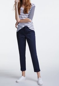 Stripet navy og hvid bomuldsbluse med trekvartærmer, parret med mørk navy tætsiddende bukser og hvide sneakers, med oprullede manchetter.