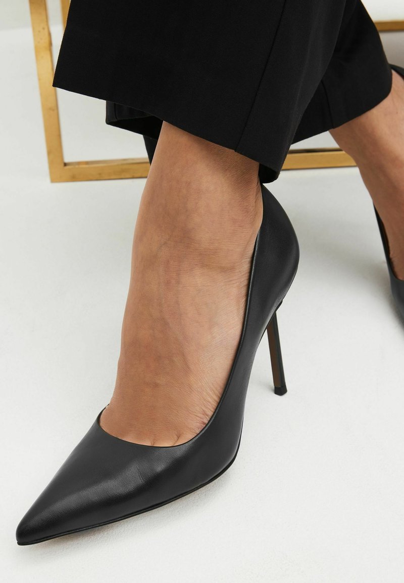 Decolté in pelle nera con tacco a spillo e punta affusolata, dal design minimalista. Presenta una texture liscia e una silhouette elegante.