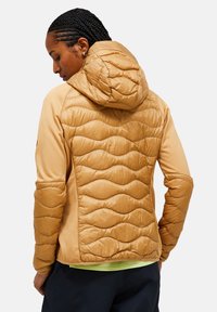 Puffjack in warm tan, met een textuur van golvende panelen op de achterkant, een capuchon en rekbare mouwen voor flexibiliteit.