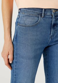 Blå denimjeans med medelhög midja, rak benklippning och klassisk femfickdesign. Har synlig sömnad och metalliska hårdvaruaccenter.
