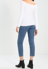 Haut blanc à manches longues côtelé avec un design épaules dénudées, associé à un jean bleu moyen longueur cheville et des bottines noires.