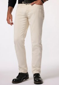 Pantalones de algodón beige con corte ajustado, bolsillos frontales y una textura sutil, combinados con zapatos de cuero negros. Con cinturón en la cintura.