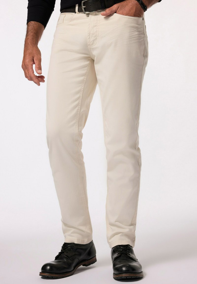 Pantalones de algodón beige con corte ajustado, bolsillos frontales y una textura sutil, combinados con zapatos de cuero negros. Con cinturón en la cintura.