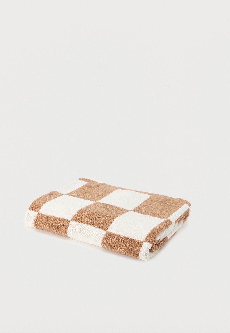 Serviette pliée avec un grand motif à damier beige et blanc, posée à plat sur une surface unie.