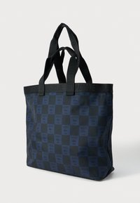 Torba na ramię w czarno-granatową kratę z podwójnymi uchwytami, ozdobiona powtarzającym się wzorem logo "Lacoste Paris" i emblematu krokodyla.