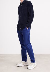 Marinblå kordjakka med bröstficka, ihopparad med blå byxor och vita sneakers. Skjortan har en knapp-down krage och strukturerad tyg.