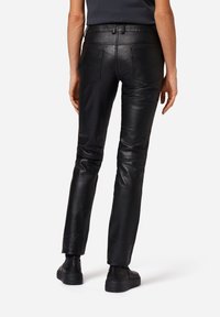 Zwarte leren broek met een slim fit, voorzien van twee achterzakken. Het materiaal heeft een gladde textuur en een subtiele glans.
