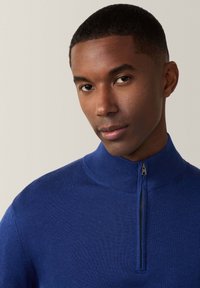 Maglione blu a maglia con colletto alto e zip a metà. Texture liscia con polsini a coste e dettagli sul colletto. Nessun motivo visibile.